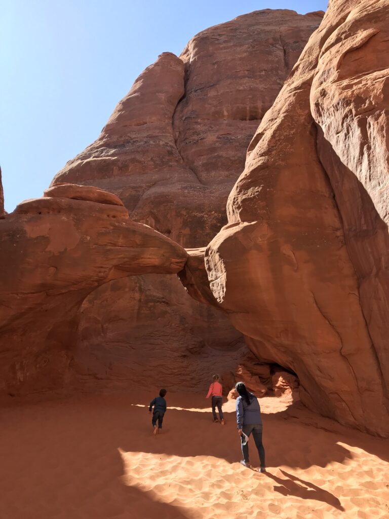 Three people walk in the sand beneath Sand Dune Arch.