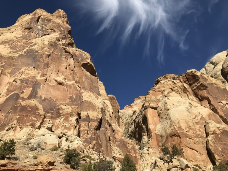 The camera is looking up at a reddish brown sandstone mountain with deep blue skies and wispy white clouds at Capitol Reef National Park.