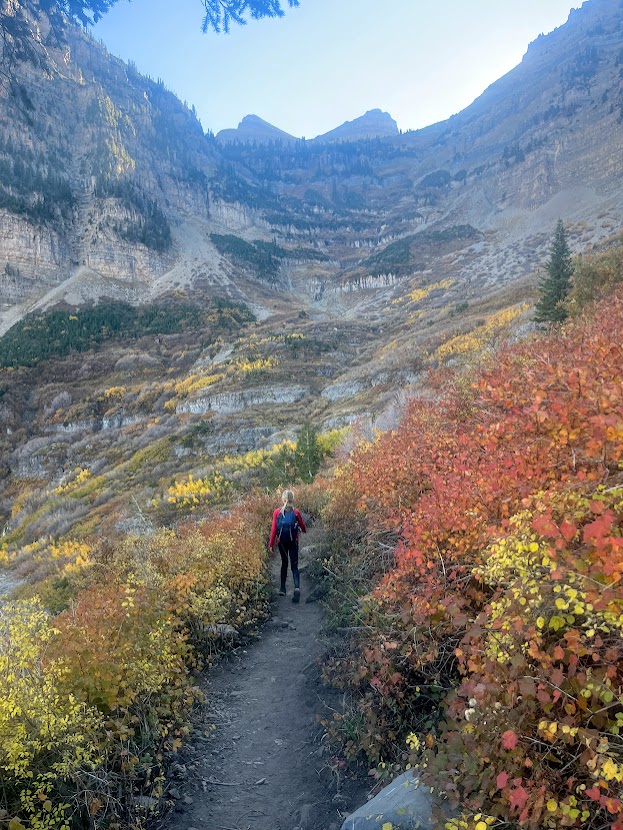 A girl walking along the Timpanogos trail surrounded by Utah fall colors of orange and yellow.