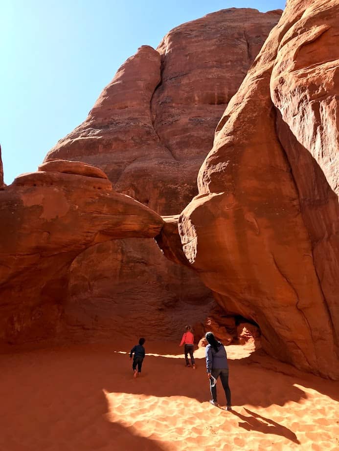 Three people walking in the soft sand at Sand Dune Arch.