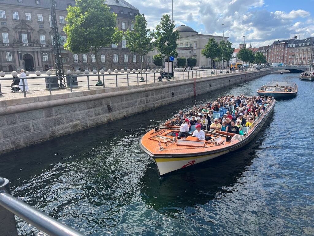 A boat full of people floats on a canal in Copenhagen on a sunny day.