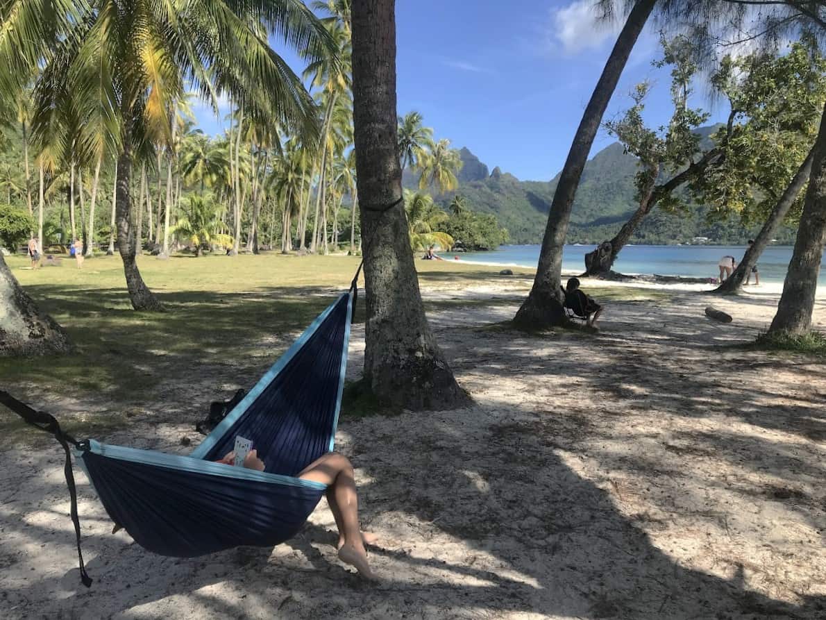 A person lays in a hammock strung between two palm trees on a the tropical beach in Moorea. It's a perfect product for the outdoors adventurer.