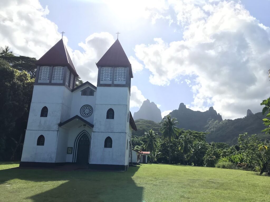 A white and red church with craggy green mountains in the background.