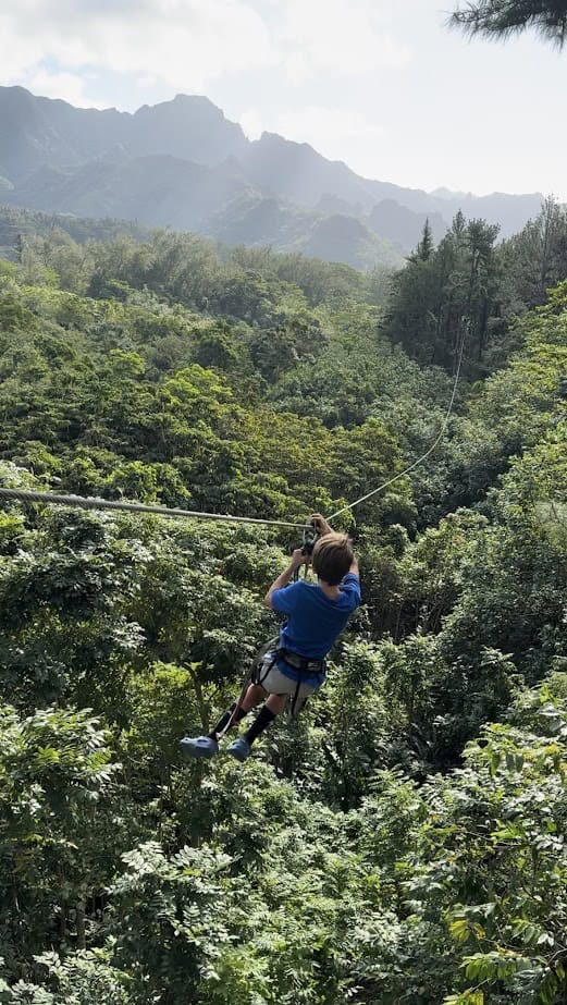 A boy ziplines through a lush forest in Moorea.