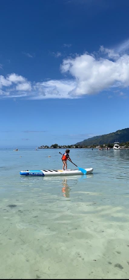 A small child is paddle boarding on clear, calm water in Moorea.