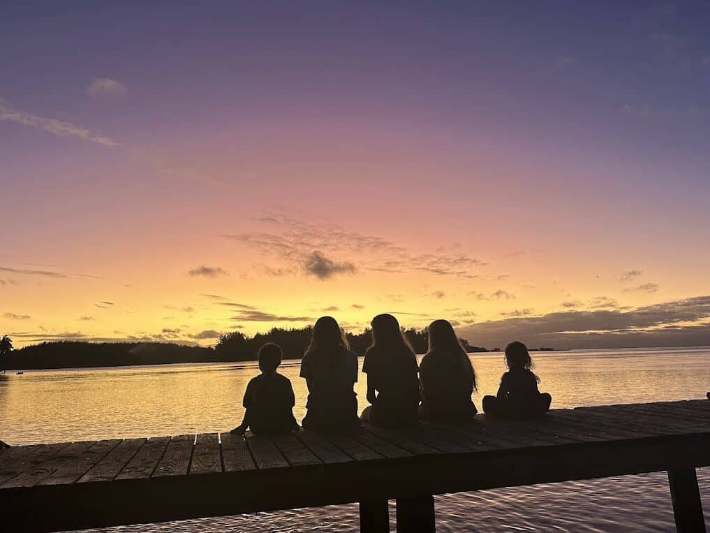 A group of people sit on a dock watching the sunset.